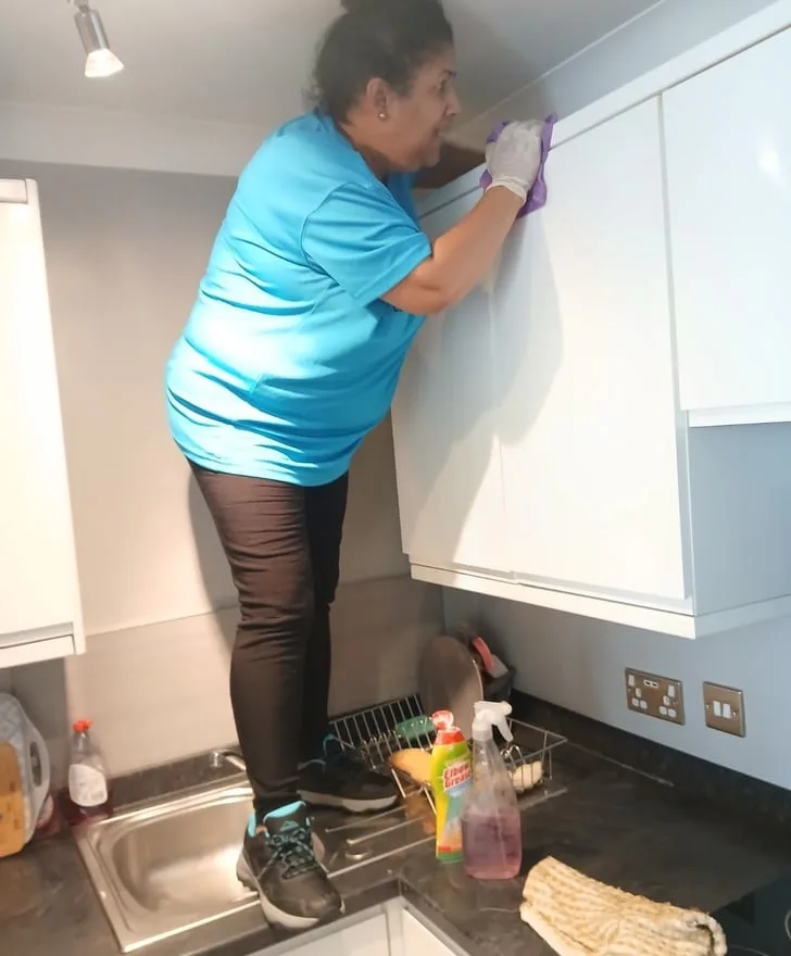 Leila cleaning the top of kitchen cupboards
